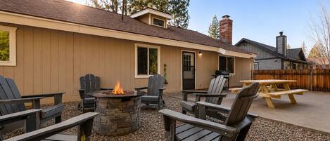 A patio area with Adirondack chairs, a stone fire pit, and a wooden table.