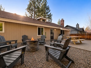 A patio area with Adirondack chairs, a stone fire pit, and a wooden table. - Eagle Point Retreat (Big Bear Lake)