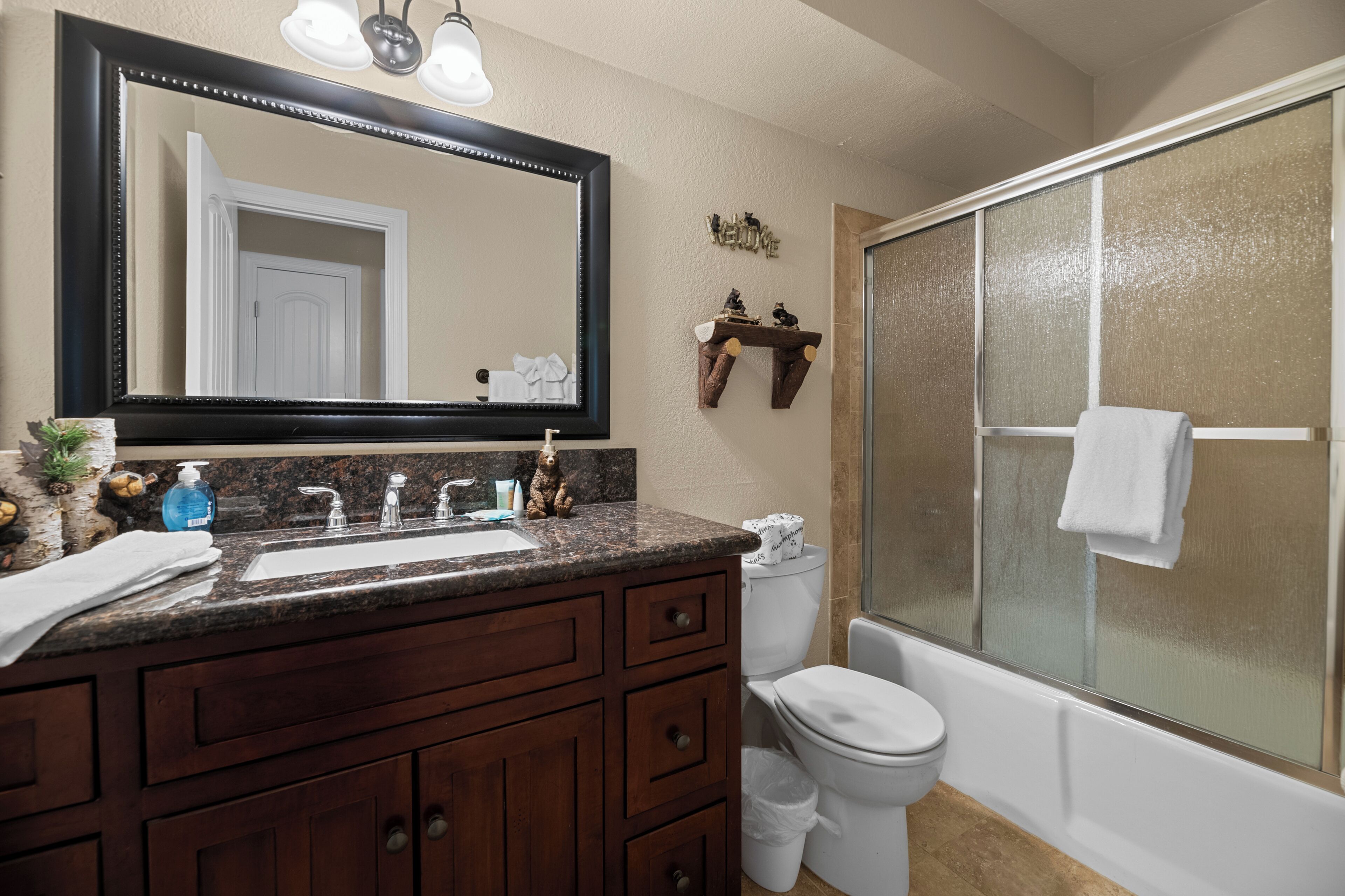 A bathroom with a large mirror, two sinks, a toilet, and a glass-enclosed shower.