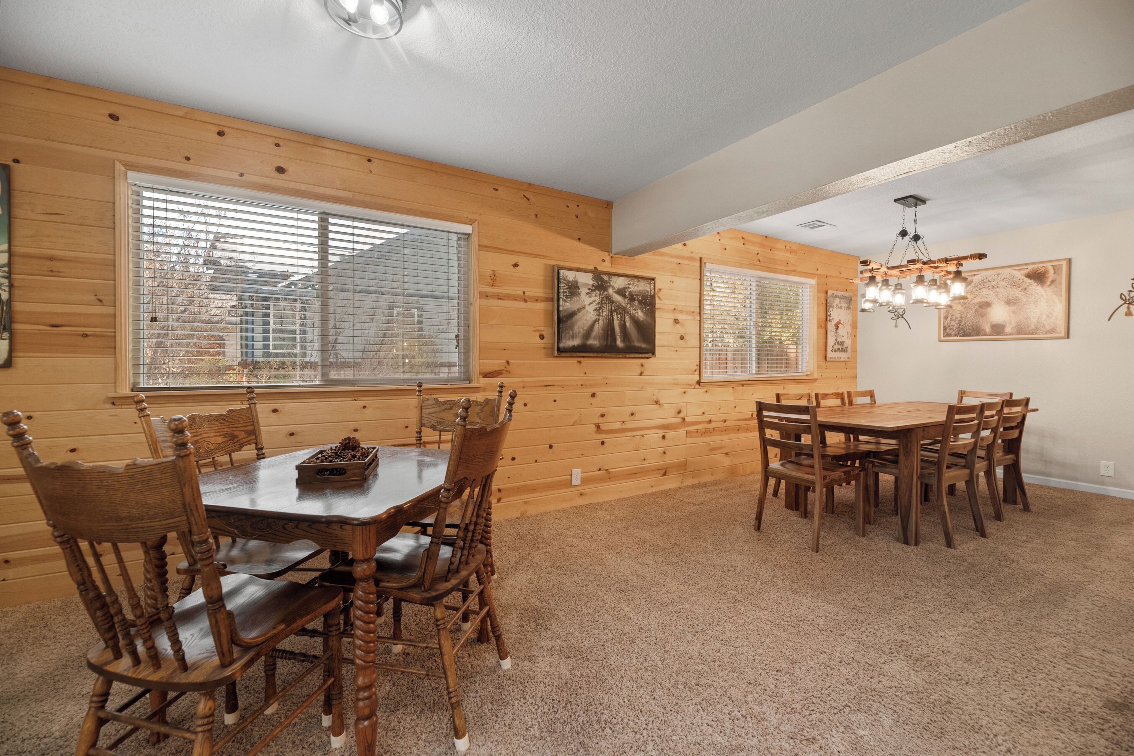 A dining area with wooden walls and a carpeted floor, featuring a round table and multiple chairs.