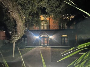 A brick building with arched windows and a central entrance, surrounded by trees and a paved pathway. - French Quarter-Style Downtown Executive Apartment (Pascagoula)