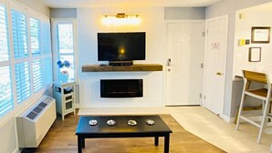 A living room with a flat-screen TV mounted above a fireplace, a coffee table, and a sofa. - Slopeside Studio Wifi Towels Ski in Out (Blue Mountain)