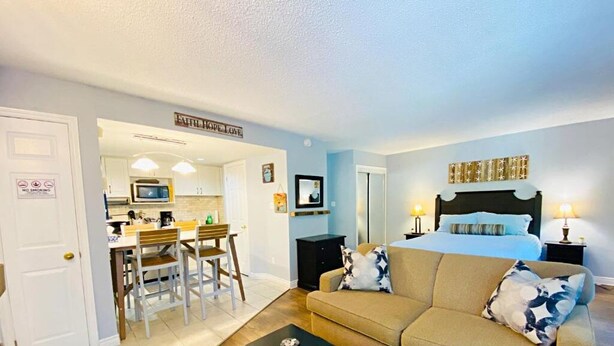 A bedroom with a bed, a sofa, a dining area with chairs, and a kitchen in the background. - Slopeside Studio Wifi Towels Ski in Out (Blue Mountain)