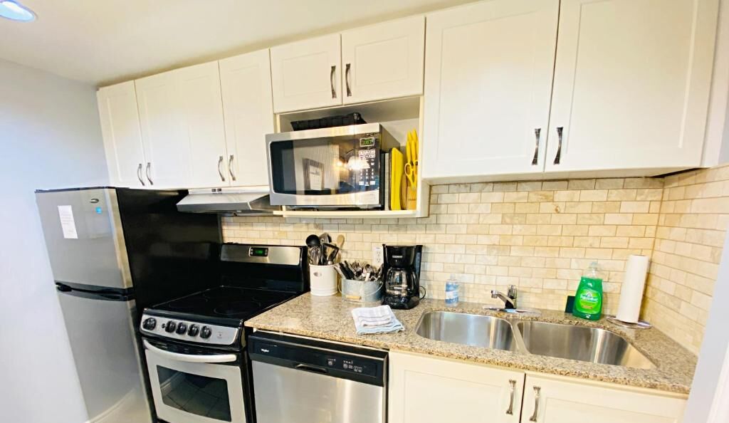 A compact kitchen with white cabinets, a stainless steel refrigerator, a microwave, a stove, and a dishwasher.