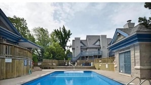 A rectangular swimming pool with a clear blue water surface, surrounded by a wooden fence and a stone wall. - Slopeside Studio Wifi Towels Ski in Out (Blue Mountain)