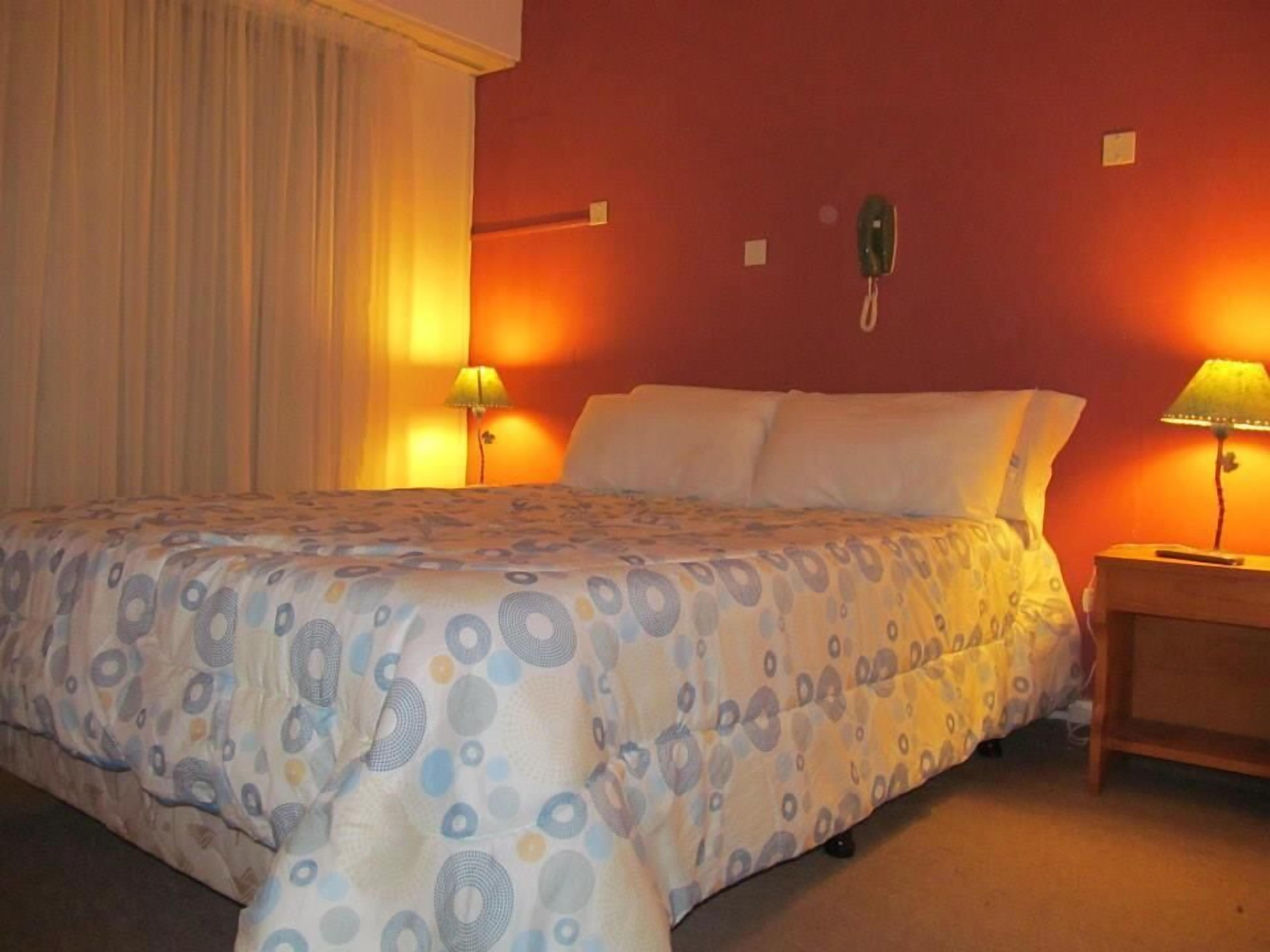 Une chambre d’hôtel avec un lit, deux lampes de chevet, un téléphone et un rideau.