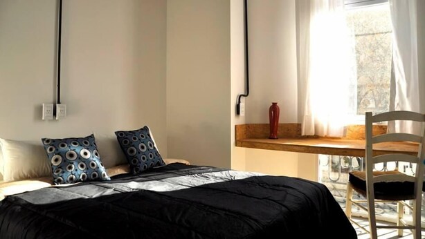 Une chambre à coucher avec un lit, deux oreillers, une table de chevet en bois, un vase rouge et une chaise.
