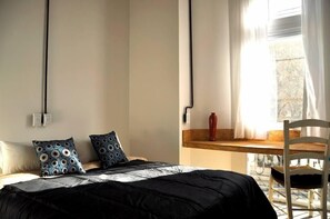Une chambre à coucher avec un lit, deux oreillers, une table de chevet en bois, un vase rouge et une chaise.