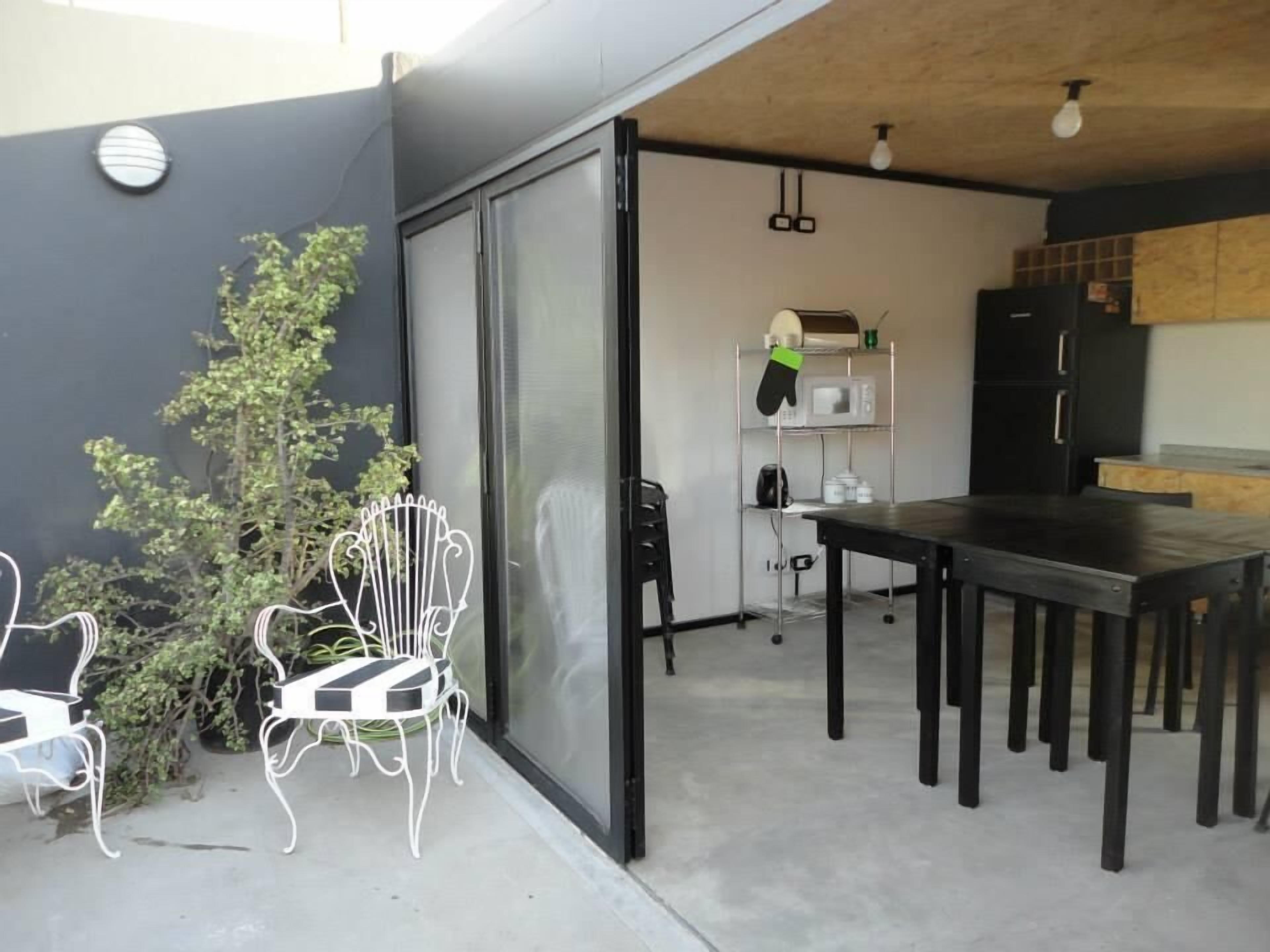A modern kitchen with a black refrigerator, a microwave, and a wooden table. There is a white chair and a potted plant outside.