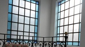 Une pièce avec un fauteuil à motifs, une balustrade en fer forgé noir et deux grandes fenêtres à carreaux.