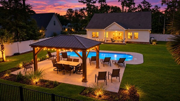 A backyard with a pool, patio furniture, and a covered seating area.