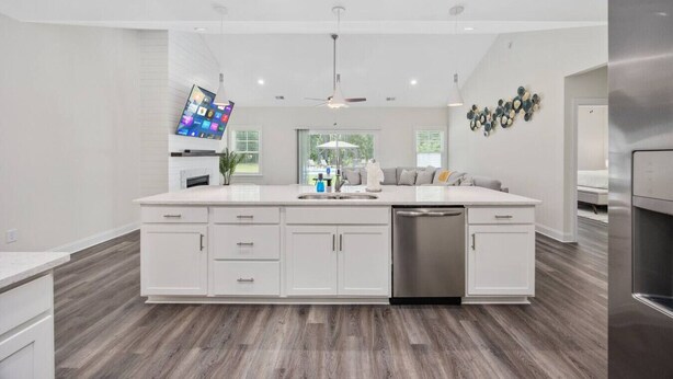 A modern kitchen with white cabinetry, a large island with a dishwasher, and a flat-screen TV mounted above the island.