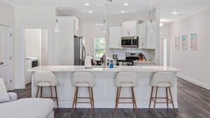 A modern kitchen with a central island, bar stools, and a dining area with a sofa.