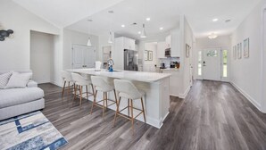 A modern kitchen with a central island, white cabinetry, and a grey sofa in the living area.