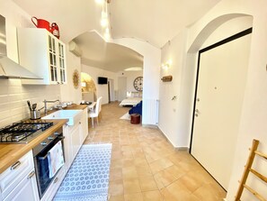 Une cuisine moderne avec une cuisinière à gaz, des armoires blanches et un coin repas agrémenté d’une chaise bleue.