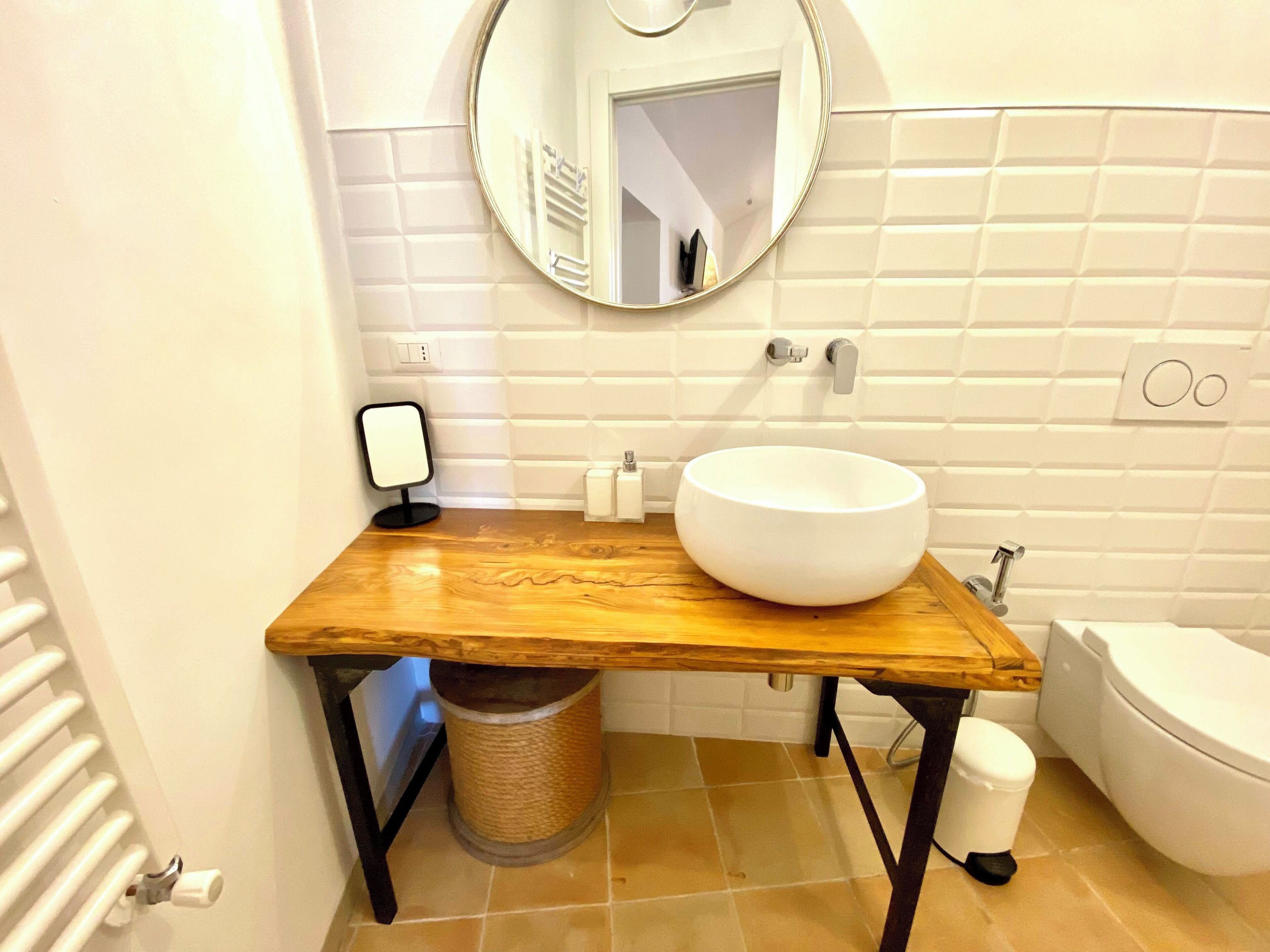 Ein Badezimmer mit einem Holz-Waschtisch, einem weißen Waschbecken, einem Spiegel und einer Toilette.