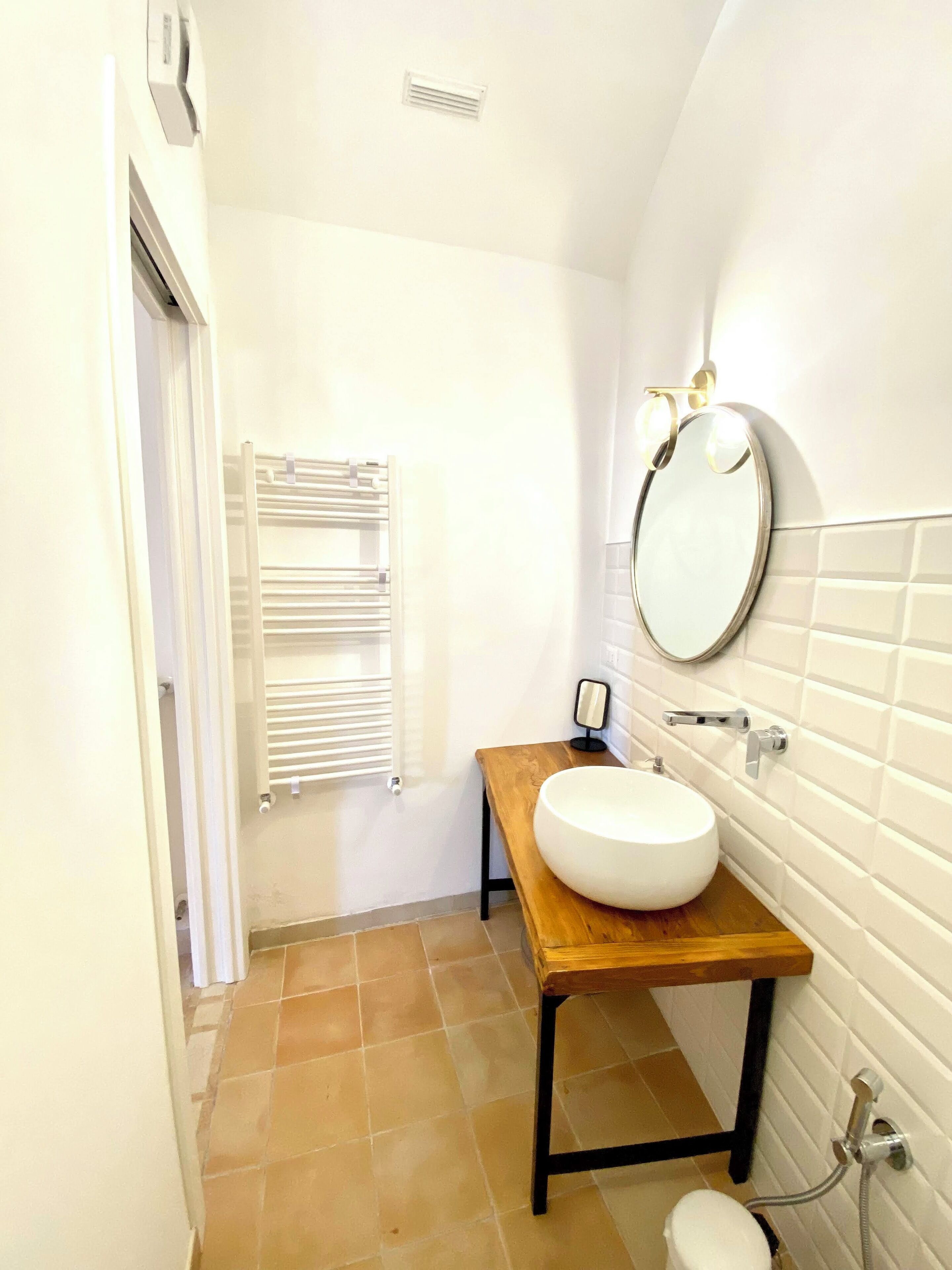 A compact bathroom with a white sink on a wooden countertop, a round mirror, a towel rack, and a shower.