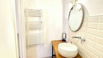 A compact bathroom with a white sink on a wooden countertop, a round mirror, a towel rack, and a shower.
