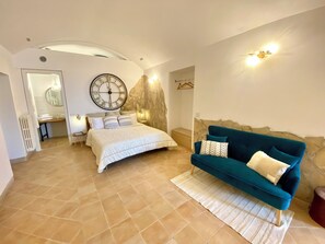 Une chambre à coucher avec un lit, un canapé bleu, une grande horloge murale et un mur décoratif en pierre.