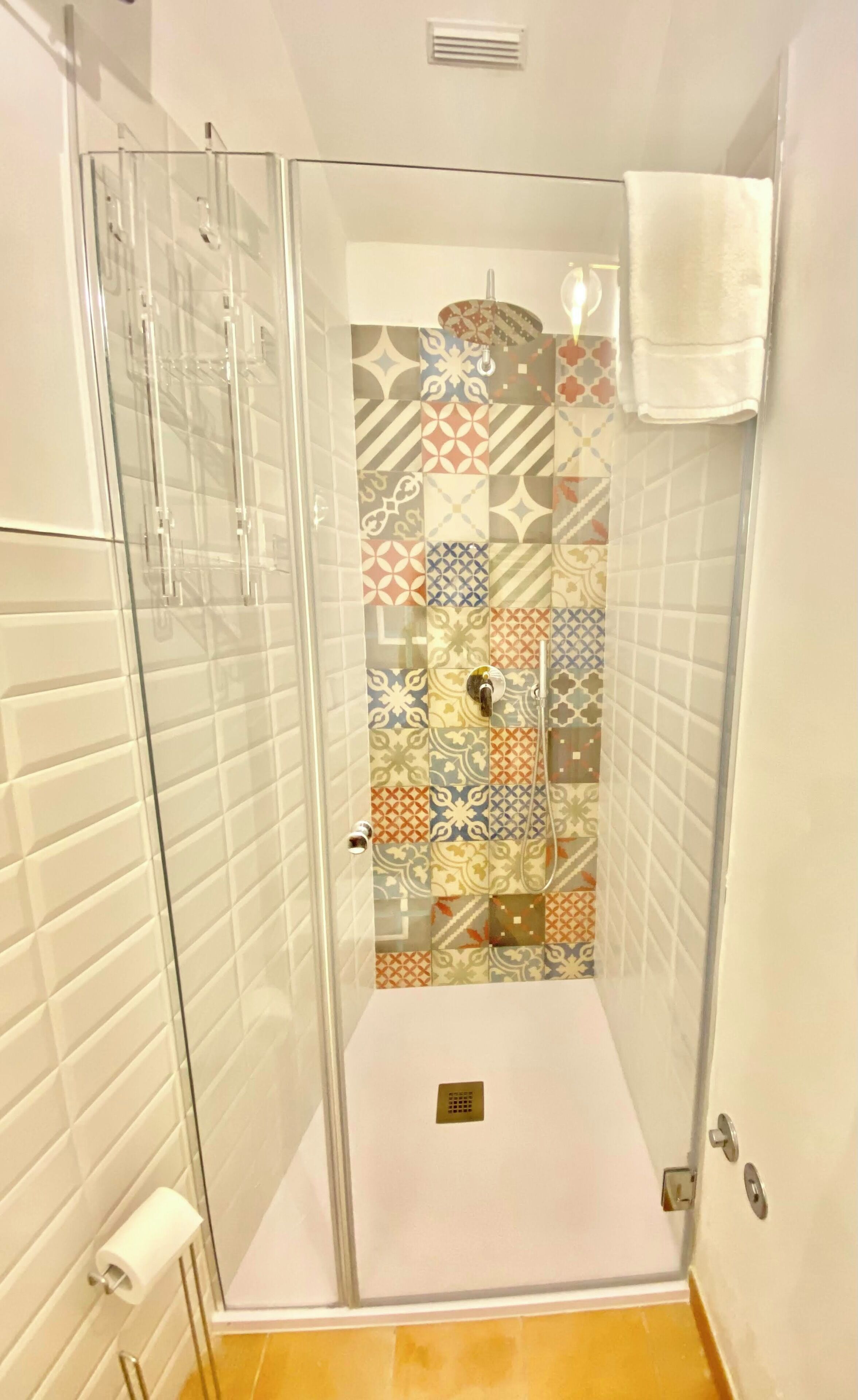 A shower with a glass door, patterned tiles, and a white towel hanging on the wall.