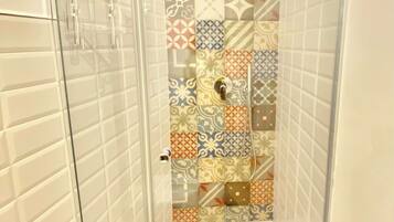 A shower with a glass door, patterned tiles, and a white towel hanging on the wall.