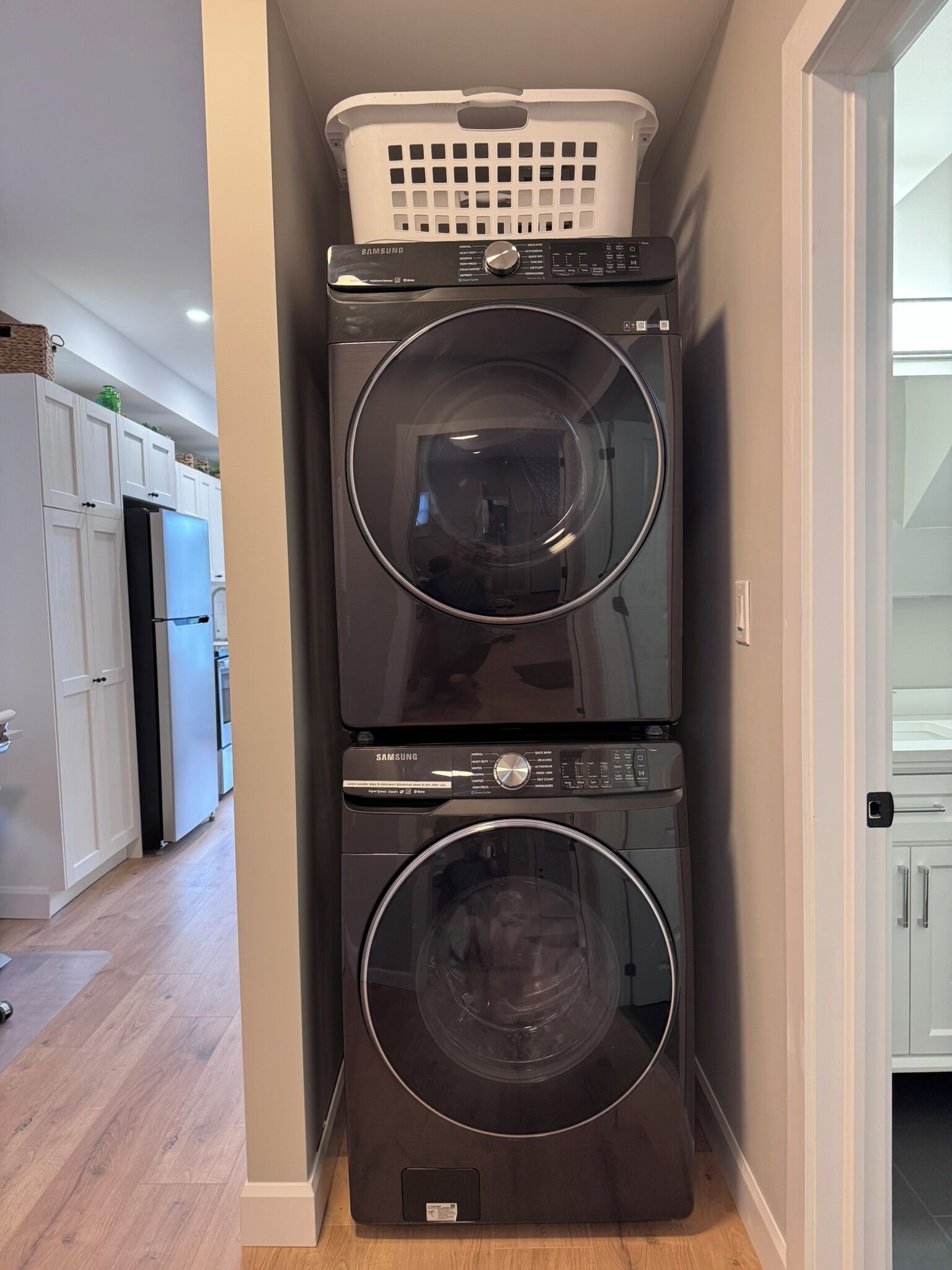 Un espace buanderie avec deux machines à laver à chargement frontal superposées et un panier à linge blanc placé sur le dessus.
