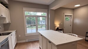 Una cocina con una isla grande, armarios blancos y una ventana con vista a una zona residencial.