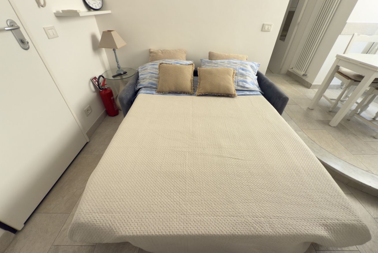 Quarto com cama, almofadas, mesa de cabeceira, abajur, extintor de incêndio e janela.