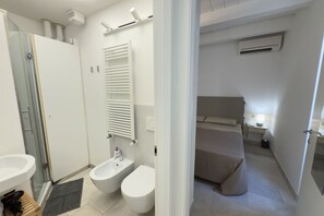 A modern bathroom with a shower, bidet, and a small bedside table with a lamp.