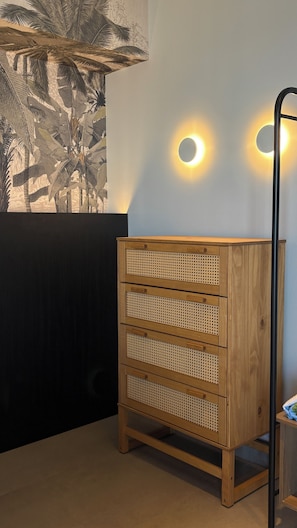 A wooden dresser with perforated drawers against a wall with a tropical plant mural.