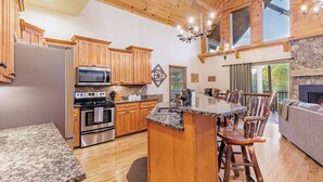 A spacious kitchen with wooden cabinets, granite countertops, a central island, and a stone fireplace. - Charming, Family-Friendly Cabin - Serene, Minutes from GSMNP Fun! Easy Access! (Whittier)