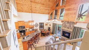 A spacious kitchen with wooden cabinets, a central island, and a stone fireplace. - Charming, Family-Friendly Cabin - Serene, Minutes from GSMNP Fun! Easy Access! (Whittier)