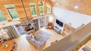 A spacious cabin with a loft bedroom, a cozy living area with a sofa and TV, and a dining area with a wooden table and chairs. - Charming, Family-Friendly Cabin - Serene, Minutes from GSMNP Fun! Easy Access! (Whittier)