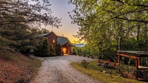 A rustic cabin with a gravel driveway leading to a wooden porch, surrounded by dense trees and a clear sky. - Charming, Family-Friendly Cabin - Serene, Minutes from GSMNP Fun! Easy Access! (Whittier)