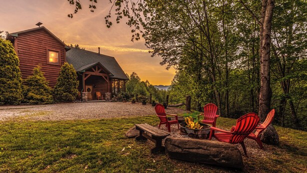 A rustic lodge with a stone fireplace, red Adirondack chairs, and a wooden table. - Charming, Family-Friendly Cabin - Serene, Minutes from GSMNP Fun! Easy Access! (Whittier)
