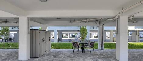 An outdoor covered patio area with a table and chairs, a grey cabinet, and a view of the street.