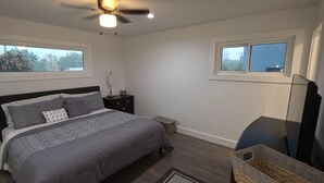 A bedroom with a bed, nightstand, TV, and windows. - Downtown Oak City Oasis (Raleigh)