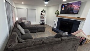 A modern living room with a sectional sofa, a fireplace, a TV mounted on the wall, and a bookshelf. - Downtown Oak City Oasis (Raleigh)