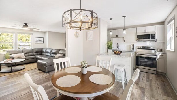 Een moderne keuken met witte kasten, een magnetron en een oven. Er is een eethoek met een ronde tafel en stoelen.