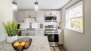 Een moderne keuken met witte kastjes, roestvrijstalen apparatuur, een granieten aanrecht en een groot raam.