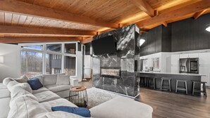 Ein modernes Wohnzimmer mit einer großen Eckcouch, einem Kamin und einer Küchenzeile mit Barhocker.