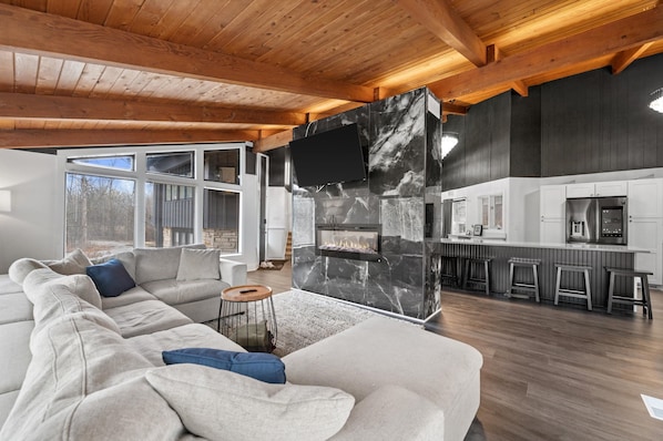 A modern living room with a large sectional sofa, a fireplace, and a kitchen area with bar stools.