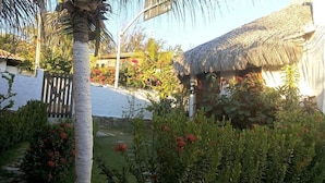 A thatched-roof hut surrounded by lush greenery and flowering plants. - Pousada Casa Castelo Bed e Breakfast (Aracati)