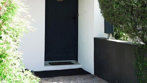 A black door with a circular window, a small step leading to the entrance, and a well-maintained hedge to the right.