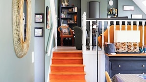 A staircase leading to a dining area with a table and chairs, a bookshelf, and a television in the background.
