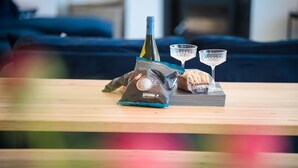A wooden table with a bottle of wine, two glasses, and a bag of snacks.