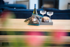 A wooden table with a bottle of wine, two glasses, and a bag of snacks.