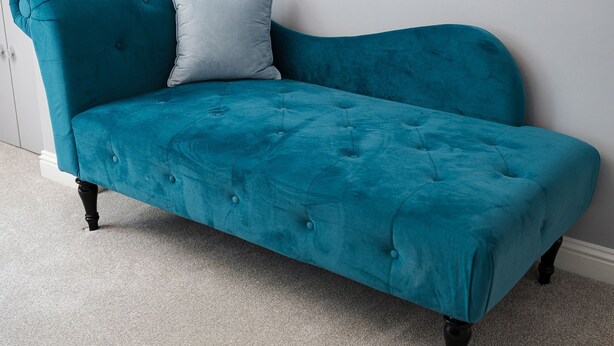 A teal velvet sofa with tufted detailing and black legs, positioned against a white wall.