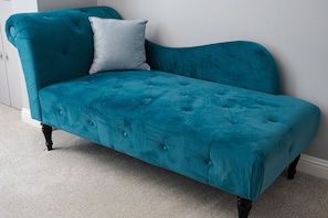 A teal velvet sofa with tufted detailing and black legs, positioned against a white wall.