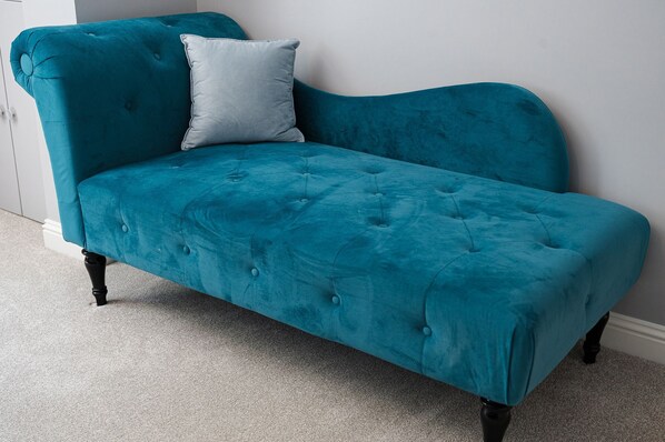 A teal velvet sofa with tufted detailing and black legs, positioned against a white wall.